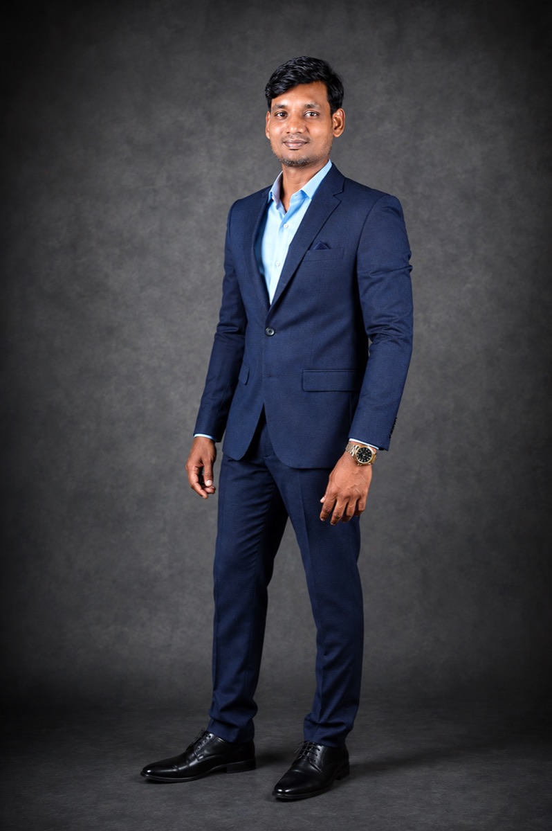 Sivaguru Arumugam, founder of Athira Share Market Academy, in a navy suit against a grey studio backdrop.
